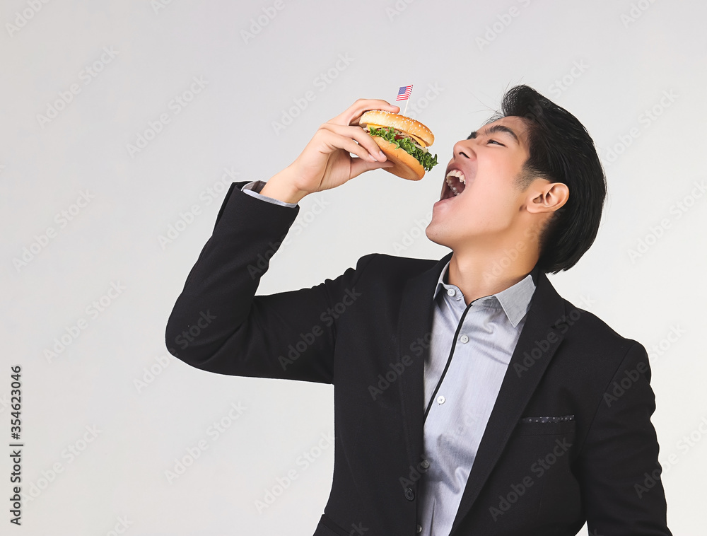 Stylish Asian young and handsome business man wearing dark suit eating burgur with American flag for Independence day.4th July. Stylish Asian young and handsome business man wearing dark suit eating burgur with American flag for Independence day.4th July.