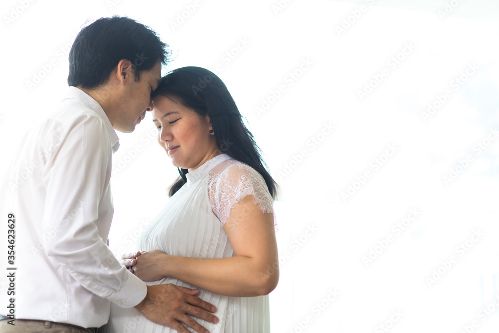 Happy Asian man hugging his pregnant wife standing at home. Love happy family concept. Pregnancy and parenthood concept. Happy Asian man hugging his pregnant wife standing at home. Love happy family concept. Pregnancy and parenthood concept.
