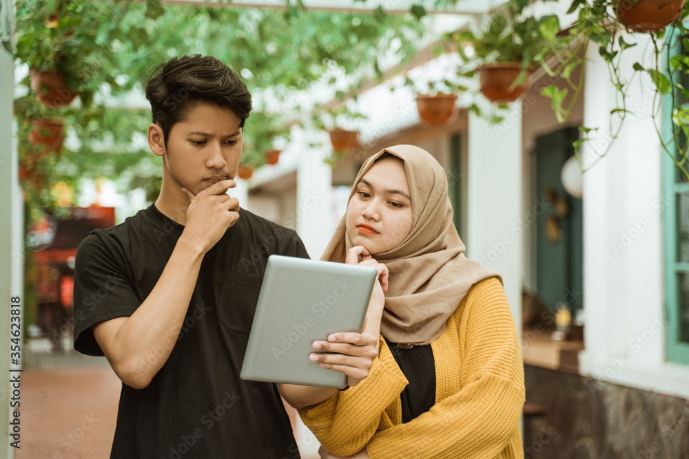 students male and hijab girl worries when looking to the screen of the tablet about wrong assignment students male and hijab girl worries when looking to the screen of the tablet about wrong assignment