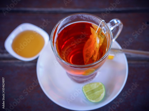 Glass of steaming black tea on saucer, with a slice of lime and honey at the side. Top view