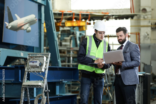 Portrait of a solid businessman with laptop and factory engineer controlling work process in a airplane manufactory. 