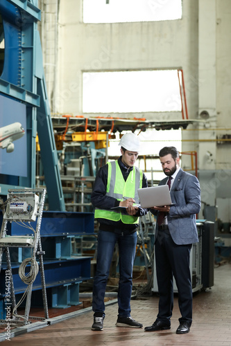 Portrait of a solid businessman with laptop and factory engineer controlling work process in a airplane manufactory. 