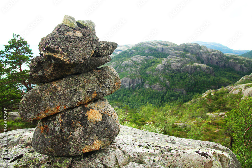 A stone troll on a rock serving as a touristic sign on a hiking trail in Norway with a green valley and mountains in the background. Serves as tourist mark at hiking trails and also is symbol of peace