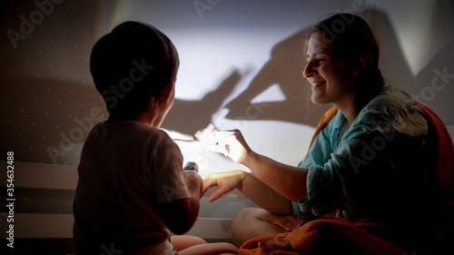 Billede på lærred Portrait of smiling young mother and little boy playing with flashlight and shad
