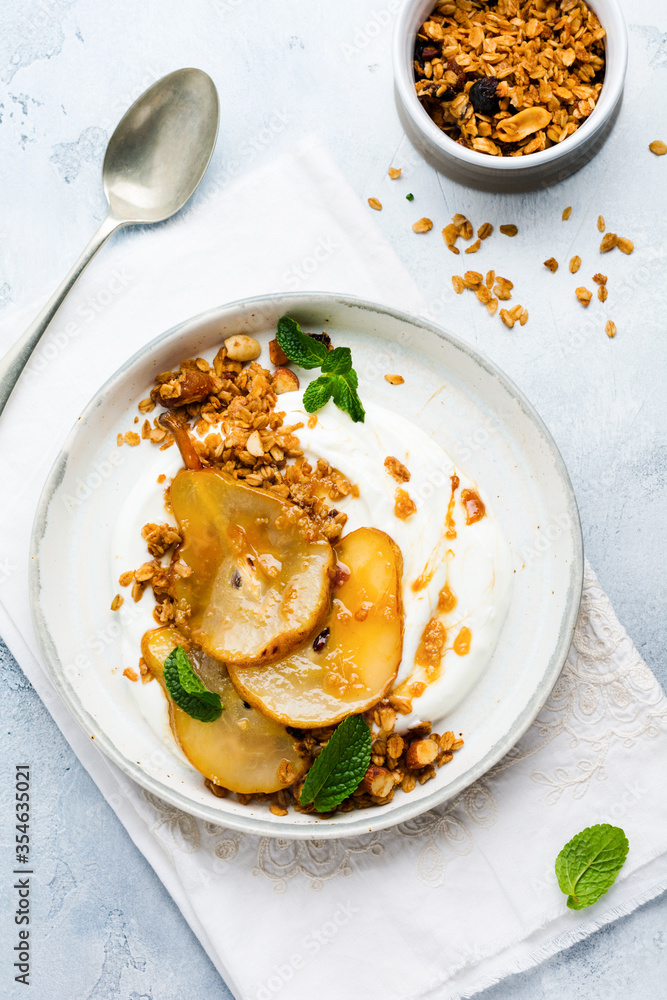 Greek yogurt with caramelized pear, granola, nuts and melted sugar for a wholesome breakfast on a gray ceramic plate. Rustic style. Top view. Greek yogurt with caramelized pear, granola, nuts and melted sugar for a wholesome breakfast on a gray ceramic plate. Rustic style. Top view.