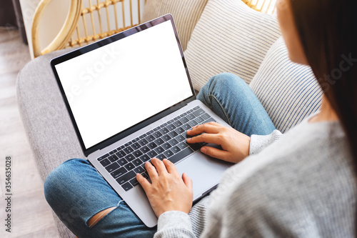 Top view mockup image of a woman working and typing on laptop computer with blank screen while sitting on a sofa at home