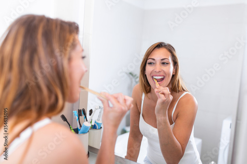 Pretty female brushing her teeth in front of mirror in the morning. Smiling young woman with healthy teeth holding a tooth brush