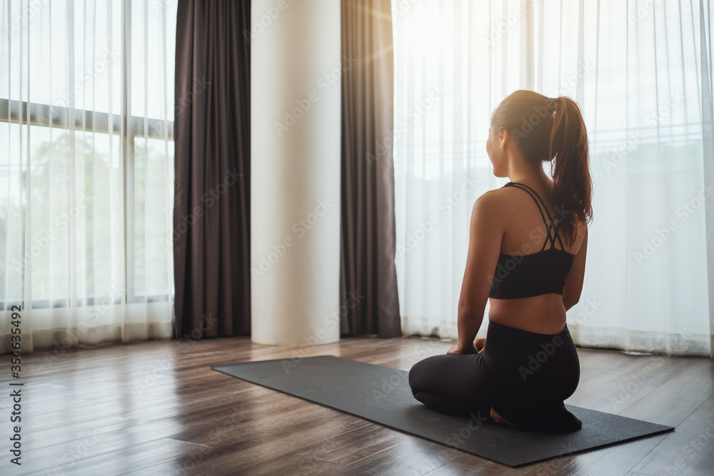 Rear view image of a beautiful young asian woman sitting on training mat preparing to workout at home Rear view image of a beautiful young asian woman sitting on training mat preparing to workout at home