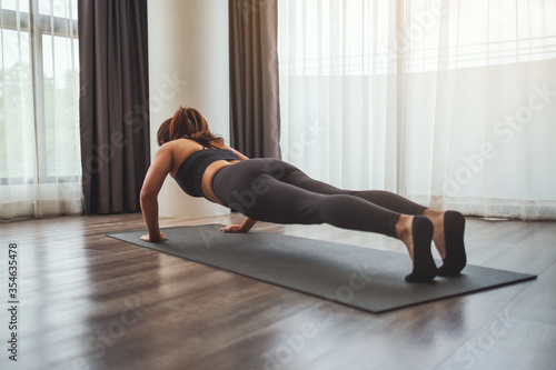 Rear view image of a young woman doing push ups on training mat at home