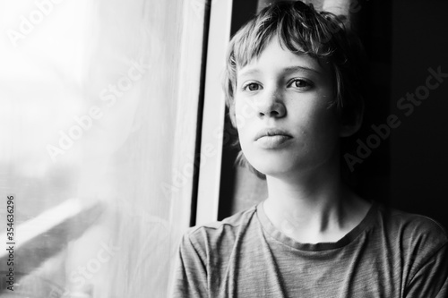 Cute 12 years old autistic boy looking through the window