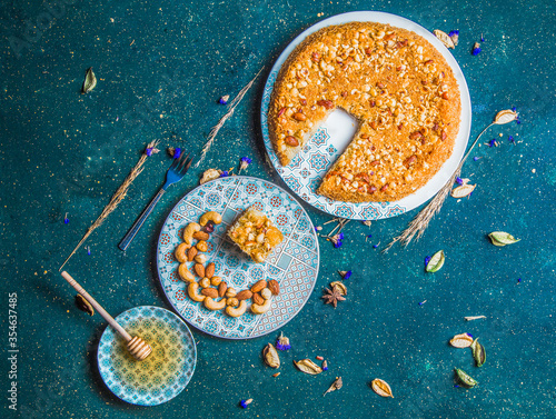 Top view of cut kadaif with nuts. Turkish kadayif with nuts on table with honey dipper and plate with piece of desert, cashew, almonds and hazelnuts. photo