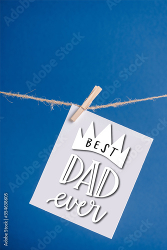 White greeting card with best dad ever illustration hanging on rope with clothespins isolated on blue
