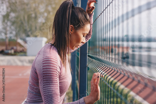 Sportswoman leaning on the fence taking a break.