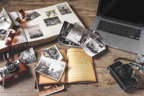 Old family photos and album on wooden background. Vintage pictures, camera, notepad and modern notebook composition. photo