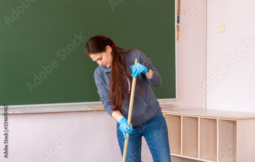 Young cleaning lady in a gray sweater and In blue gloves. She mops the floor.