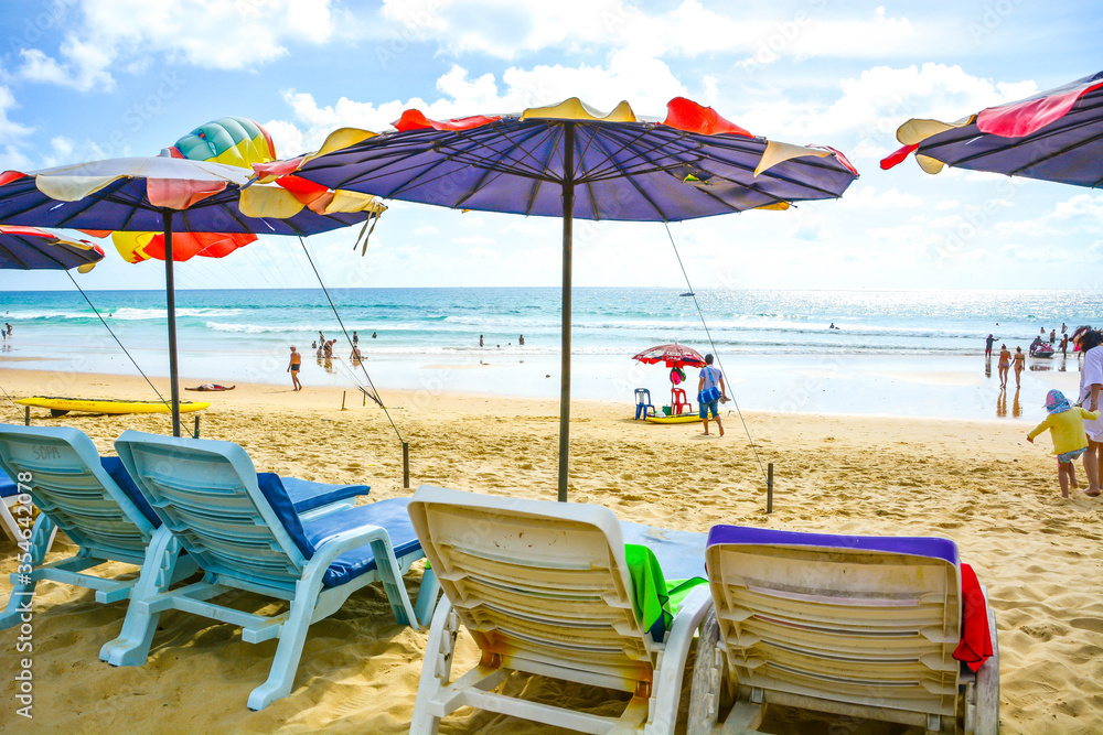 People going to beach under bright sunny sky with benches and colorful beach umbrella by the sea, Phuket, Thailand. Summer beach activity background
