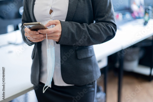 Business woman in a white shirt has taken off a medical mask and is typing on a smartphone. Faceless female office clerk texting over a break at work. End of quarantine. Victory over the coronavirus. © Михаил Решетников