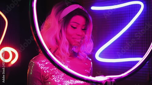 Model posing in neon lights spend time relaxing dancing on camera. African American girl dancing in photo studio in neon abstract figure lighting in a silver shining dress. Neon concept. Prores 422. 