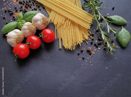 Traditional Italian cuisine. Basic ingredients for cooking pasta in the form of the Italian flag: basil, garlic, tomato, rosemary, spaghetti, peppercorn. Italian food, dark background, copy space.