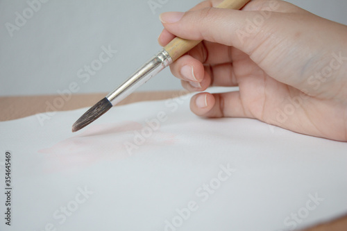 Hand holding paint brush on paper. Artist paints a picture.