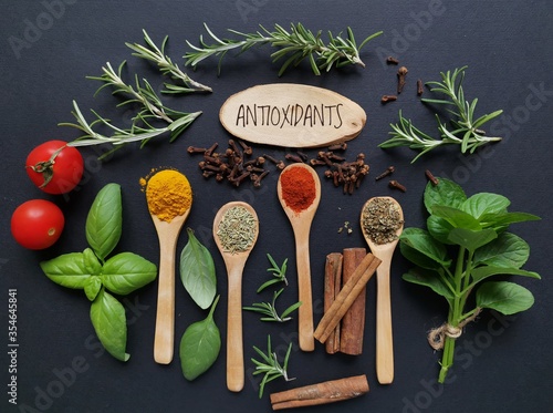 Set of various spices in wooden spoons with fresh herbs. Natural sources of antioxidants rosemary twigs, fresh green basil leaf, mint leaf, turmeric, clove, cinnamon, chili, tomato. photo