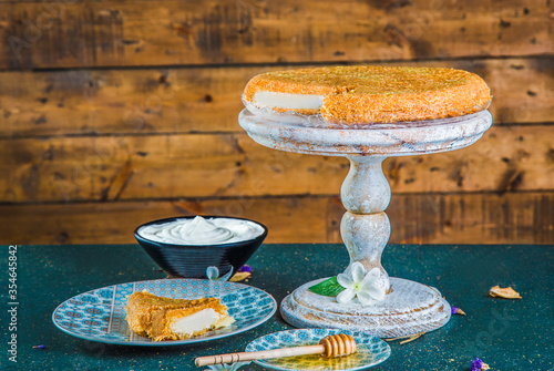 Arabic dessert of kunefe on antique stand with missing piece. Cut oriental dessert with cream cheese and kadayif on cake stand with wooden background.