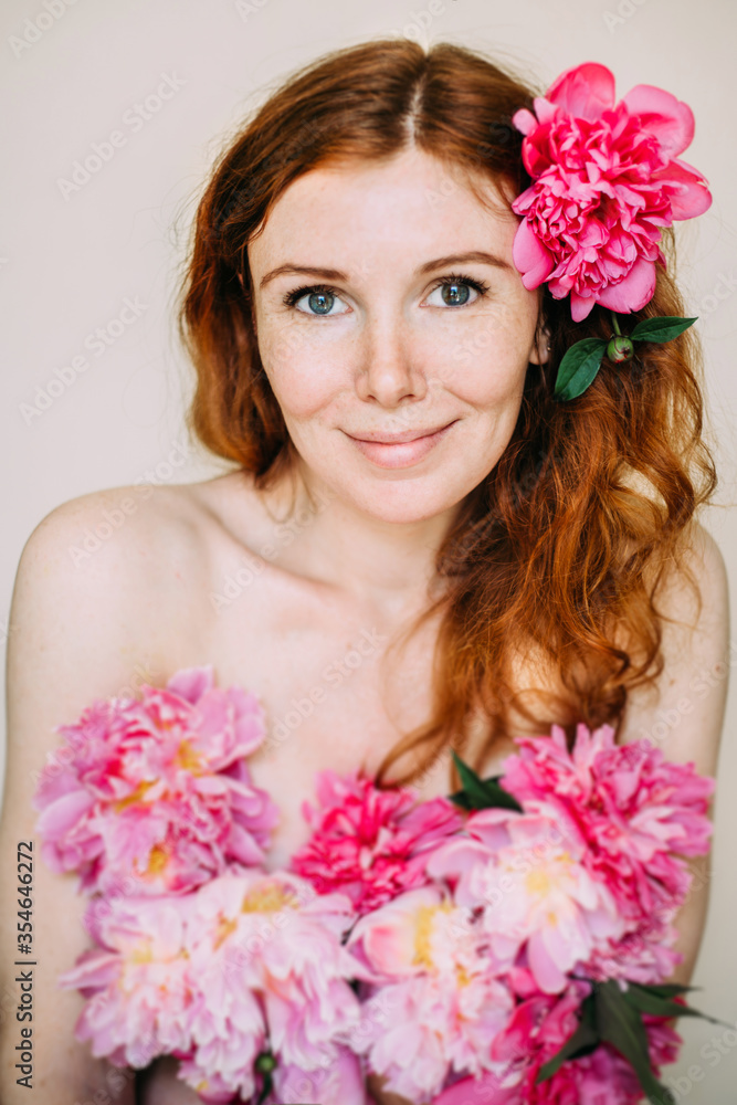 Redhead girl with freckles dressed in pink peonies flowers as in a dress with naked shoulders. Natural beauty. The concept of self-love and appearance. Redhead girl with freckles dressed in pink peonies flowers as in a dress with naked shoulders. Natural beauty. The concept of self-love and appearance.