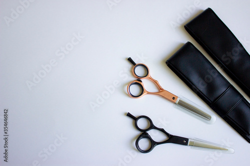 Hairdressing scissors. For cutting and milling. Black and rose gold. Next to the covers of leather and caps tips on the blade. Solid white background. Base, banner, postcard. photo