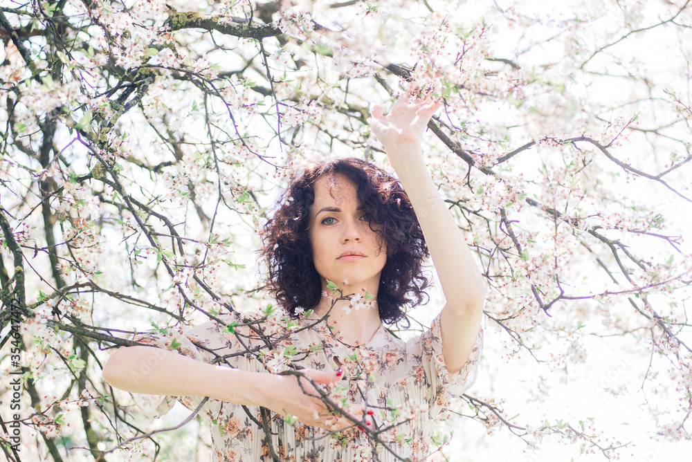 Young attractive woman with curly long hair posing in spring blooming garden, apple trees Young attractive woman with curly long hair posing in spring blooming garden, apple trees