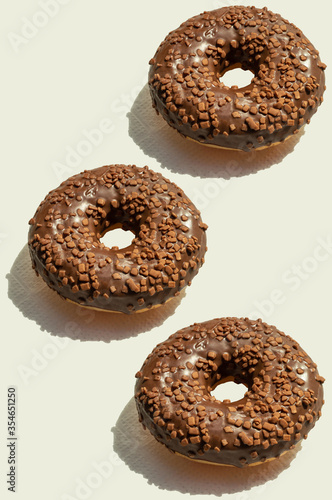 Three chocolate donats with sunny shadows on vertical background. Fresh delicious desserts. Creative food pattern, top view. Geometrical trendy concept idea