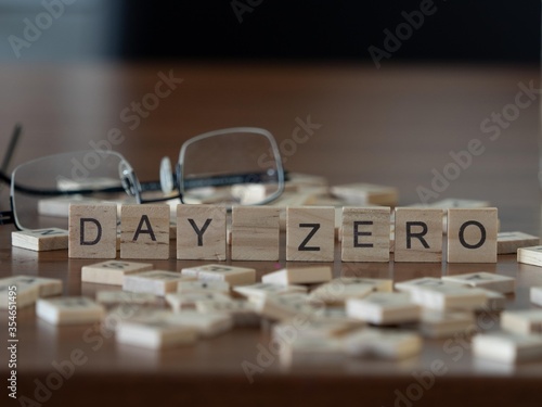 day zero concept represented by wooden letter tiles on a wooden table with glasses and a book