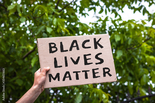 Hand holding cardboard banner with text Black Lives Matter. Anti-racism protest. © hardvicore