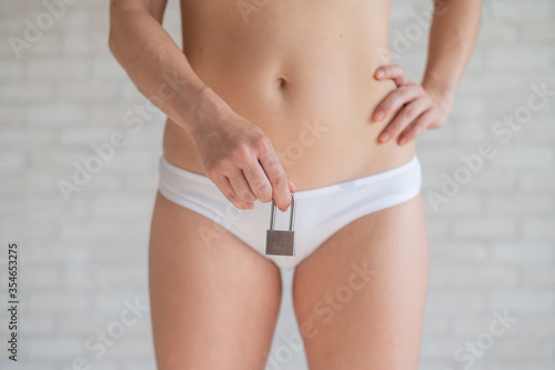 The concept of women's purity and innocence. Slender faceless woman with naked belly dressed in white panties holding a padlock. Bans on menstruation.