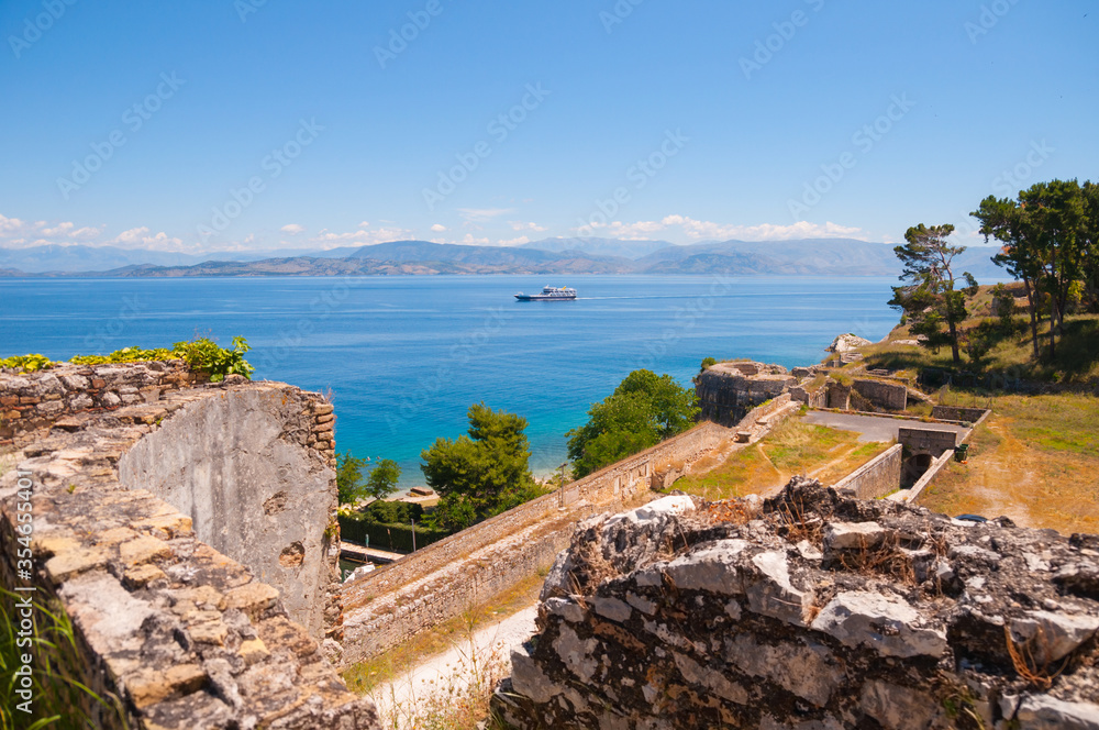 View from ancient fortress ruins to a sea with ship and other shore with mountains at the horizon