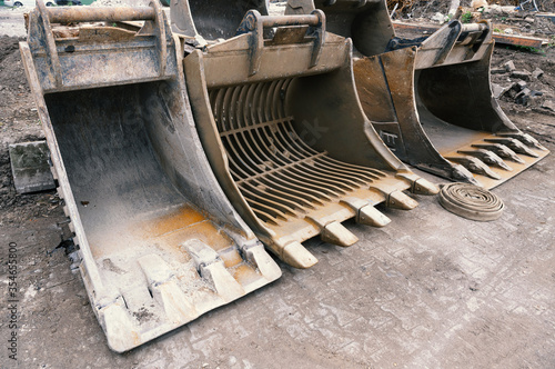 Large used excavator shovels stand side by side on a cement floor.