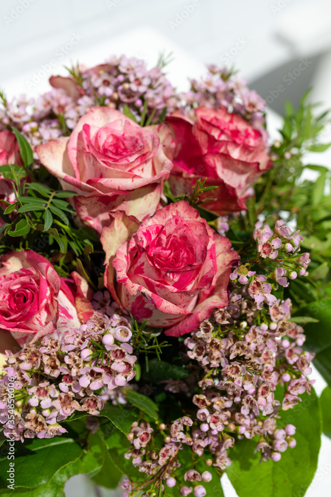 A decorative bouquet of red and white spotted roses with decorative green.