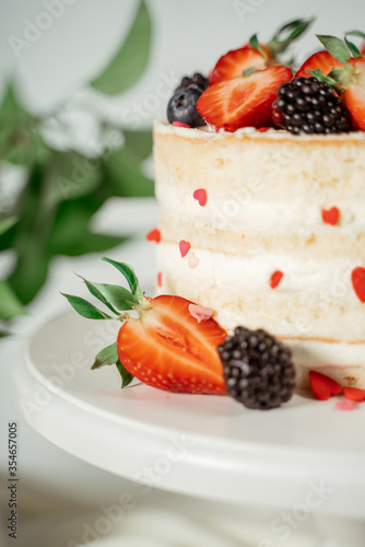 Fototapeta Naklejka Na Ścianę i Meble -  White berry cream cake decorated with strawberries and blackberries, among lilac flowers and green leaves. Food photography. Advertising and commercial close up design.