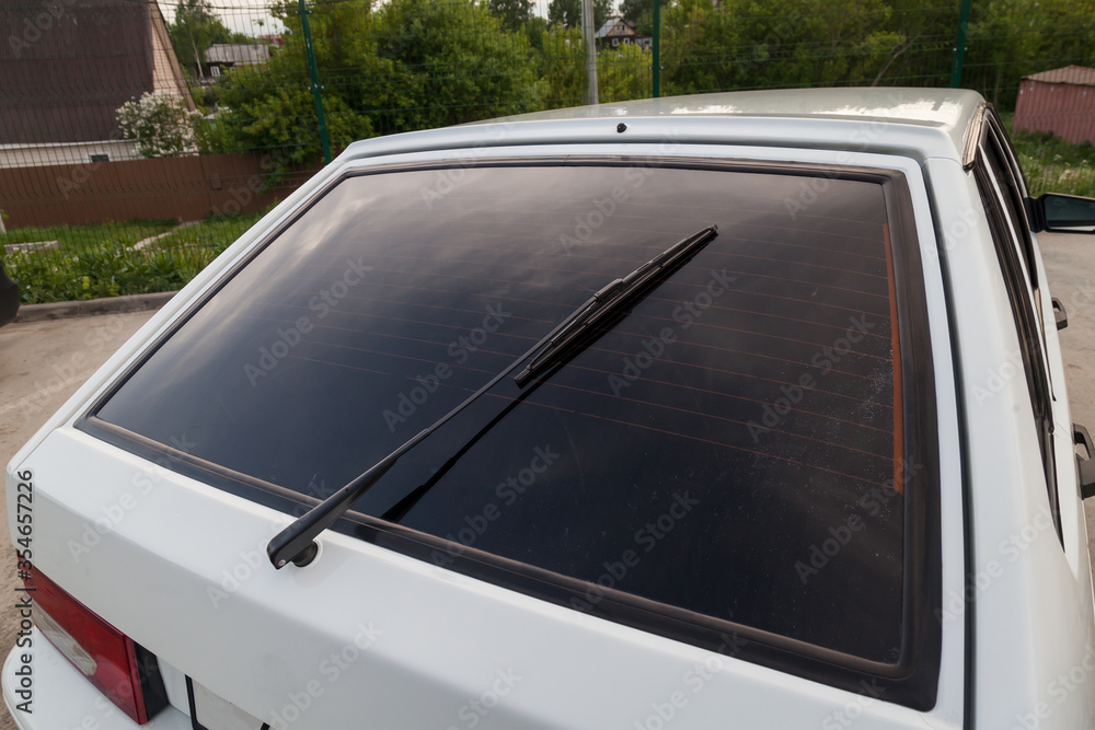 Obraz premium Closeup of a clean rear tinted black glass of a Russian white car with a wiper and a red brake light. Presale preparation of a auto after washing.