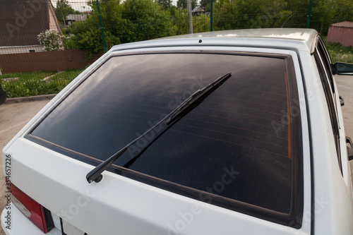 Closeup of a clean rear tinted black glass of a Russian white car with a wiper and a red brake light. Presale preparation of a auto after washing. photo