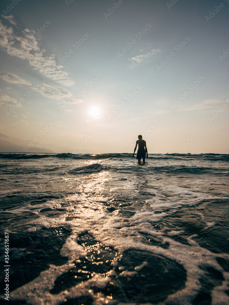 Lonely man walking into the sea during sunset