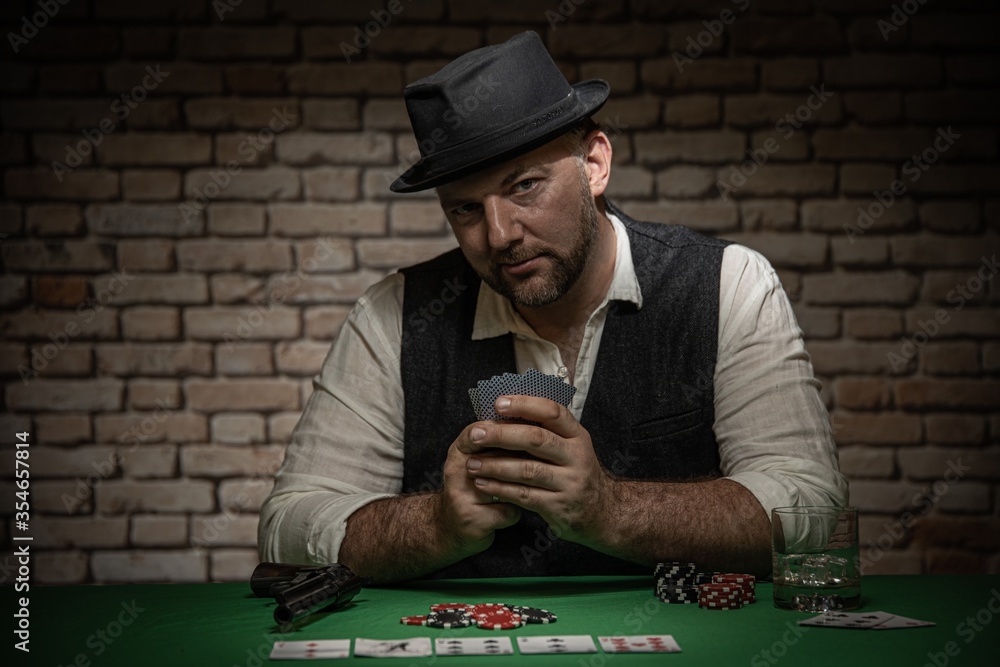 Poker player with cards and playing chips a the poker table - poker in a dark back room with a brick wall Poker player with cards and playing chips a the poker table - poker in a dark back room with a brick wall