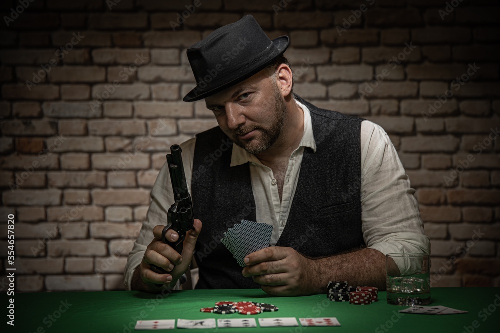 Poker player sitting behind the poker table with cards and playing chips - poker in a dark back room with a brick wall Poker player sitting behind the poker table with cards and playing chips - poker in a dark back room with a brick wall