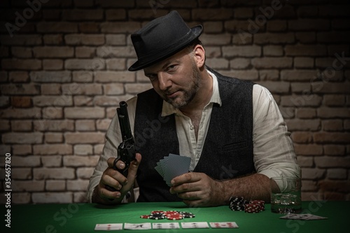 Poker player sitting behind the poker table with cards and playing chips - poker in a dark back room with a brick wall