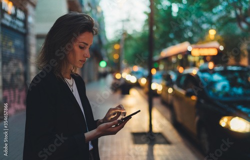 Traveler woman calling mobile phone waiting yellow taxi in evening street europe city Barcelona. Girl tourist using smartphone internet online gadget cellphone on background bokeh headlights of cars