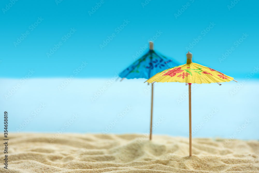 Sun umbrellas on sandy beach with blurry blue ocean and sky. Summer background. Soft focus