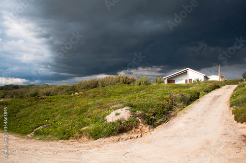 Dark thunderclouds over the small white house with red roof on the rocky hill. A storm is coming