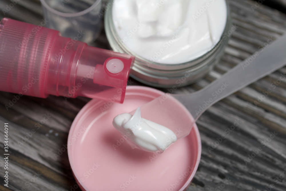 Plastic bottle with cream. The cover is removed and lies nearby. Near the shoulder blade, on it a cream. Against the background of pine boards. Plastic bottle with cream. The cover is removed and lies nearby. Near the shoulder blade, on it a cream. Against the background of pine boards.