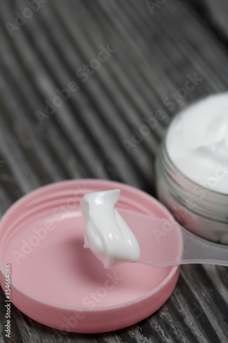 Plastic bottle with cream. The cover is removed and lies nearby. Near the shoulder blade, on it a cream. Against the background of pine boards.