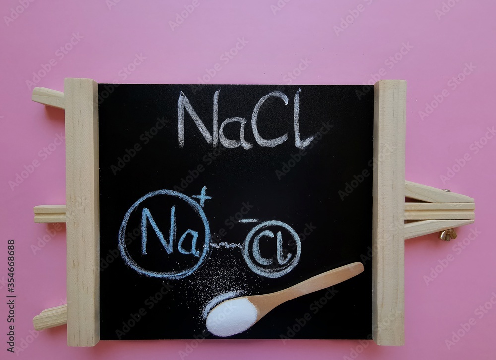 Structural chemical formula of sodium chloride molecule on a black chalkboard with spoonful of