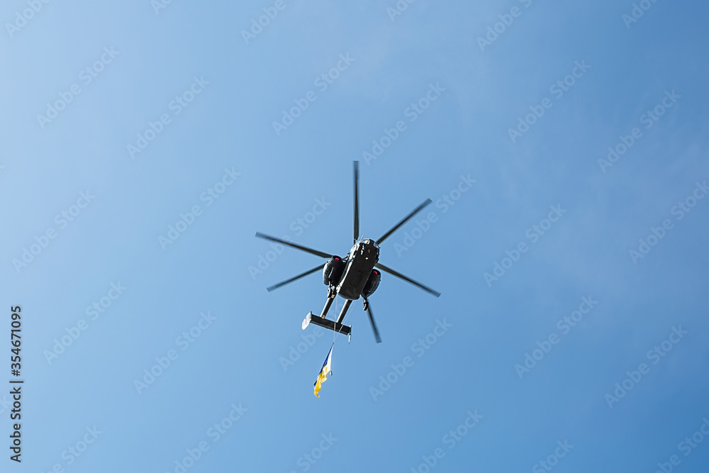Fototapeta premium Small civil helicopter with Ukrainian flag flies against a blue sky with clouds background